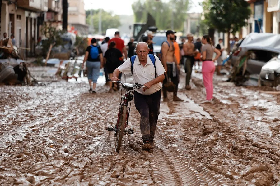 Un vecino de Paiporta atraviesa con su bicicleta una calle cubierta de barro. EFE/Biel Aliño